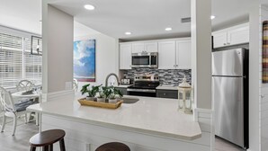 A modern kitchen with white cabinetry, a stainless steel refrigerator, and a central island with bar stools. - Cozy 1BR Villa w/ Lagoon Views (Hilton Head Island)
