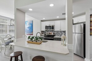 Een moderne keuken met witte kastjes, een roestvrijstalen koelkast en een centraal kookeiland met barstoelen.
