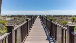 Une promenade en bois qui mène à une plage, avec un ciel dégagé.