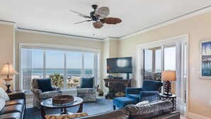 A spacious living room with a large window overlooking the beach, a ceiling fan, and a flat-screen TV. - Direct Ocean Front Villa w/ Large Balcony (Hilton Head Island)