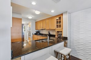 A modern kitchen with wooden cabinets, a granite countertop, a stainless steel sink, and a bar stool.