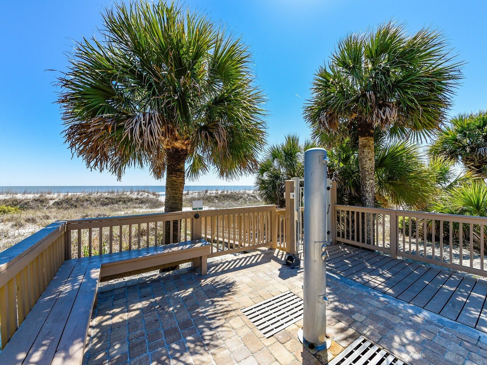 A wooden deck with a bench, palm trees, and a view of the beach.