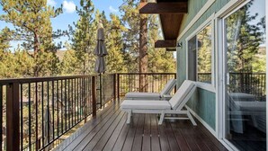 Une terrasse en bois avec une rambarde, un espace couvert avec une table et des chaises, et une vue sur les arbres.