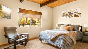 Une chambre à coucher comprenant un lit, une chaise, une petite table, une fenêtre donnant sur un paysage agréable et des œuvres d’art accrochées au mur.