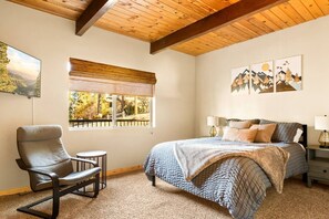 Une chambre à coucher comprenant un lit, une chaise, une petite table, une fenêtre donnant sur un paysage agréable et des œuvres d’art accrochées au mur.