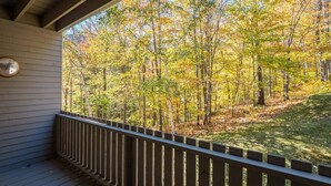 A covered porch with a wooden railing overlooking a forested area. - Ski-In/Ski-Out Sunday River Condo: Sunrise A-104 (Newry)