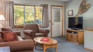 A furnished room with a sofa, armchairs, a television, and a door. - Ski-In/Ski-Out Sunday River Condo: Sunrise A-104 (Newry)