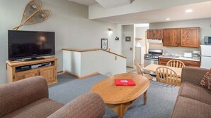 A living room with a TV, sofa, and dining table. - Ski-In/Ski-Out Sunday River Condo: Sunrise A-104 (Newry)