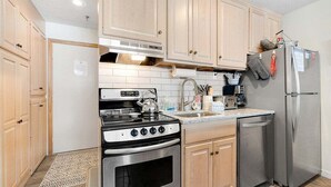 Cocina compacta con armarios de madera, estufa de acero inoxidable, lavavajillas y refrigerador.