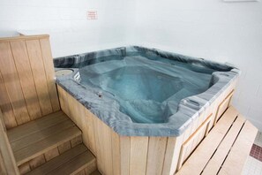 A hot tub with wooden steps and a tiled floor.