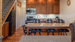 A kitchen with wooden cabinets, a stainless steel refrigerator, a built-in oven, a granite countertop, and a dining area with four chairs.