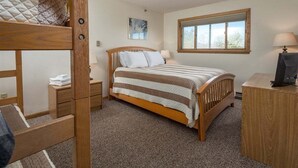A bedroom with a bunk bed, a single bed, a bedside table with a lamp, a desk with a computer, and a window with a view.