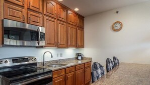 A kitchen with wooden cabinets, a stainless steel oven, granite countertops, and a clock on the wall.