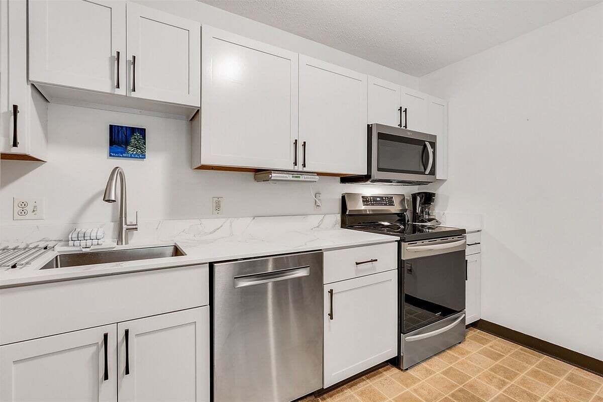 A modern kitchen with white cabinets, stainless steel appliances, and a tiled floor.