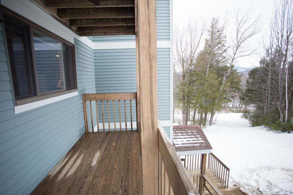 Une terrasse en bois avec un banc, une fenêtre et une vue sur les arbres et la neige.