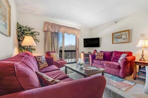Ein Wohnzimmer mit zwei violetten Sofas, einem Couchtisch, einem Fernseher und einem Fenster mit Vorhängen.