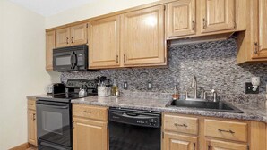 Una cucina con mobili in legno, un piano di lavoro in granito, un forno a microonde, un tostapane, un lavello e una lavastoviglie.