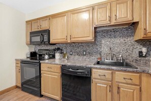 A kitchen with wooden cabinets, a granite countertop, a microwave, a toaster, a sink, and a dishwasher.
