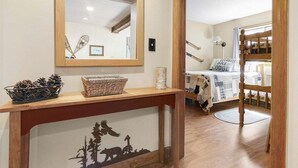 Una stanza con un letto, un tavolino consolle in legno con un cesto e un oggetto decorativo, uno specchio e un letto a castello sullo sfondo.