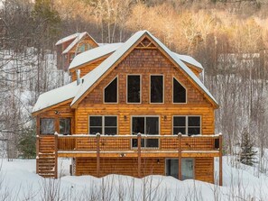 A log cabin with a balcony, surrounded by snow and trees.