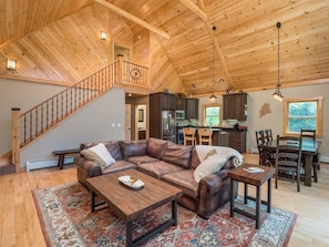 A spacious living area with a wooden ceiling, a leather sofa, a dining table, and a kitchen in the background.