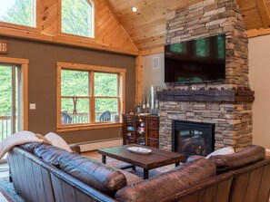 A cozy living room with a stone fireplace, leather sofa, and a flat-screen TV.