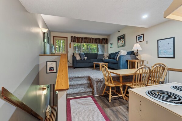 A compact living space with a dining area, sofa, and a staircase leading to an upper level.