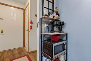 Una cocina con microondas, cafetera y un estante con varios objetos.