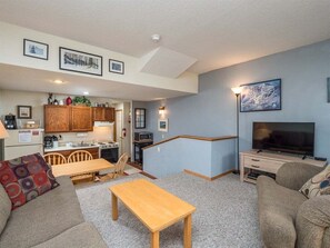 A compact living space with a kitchenette, a dining area, a sofa, a TV, and artwork on the walls.