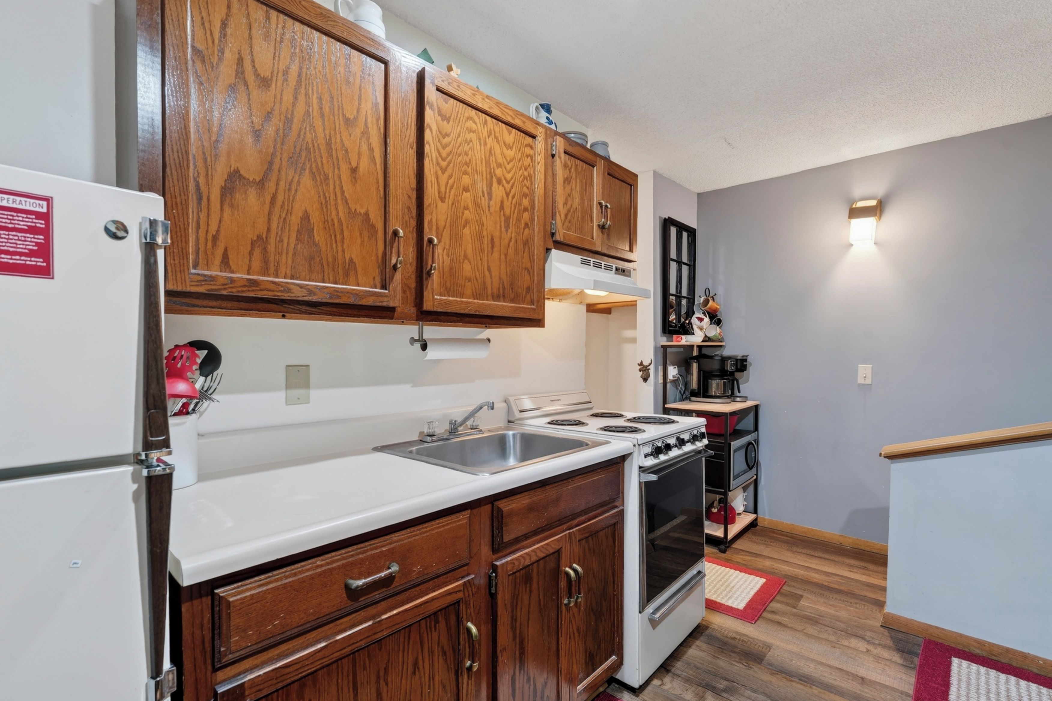 A compact kitchen with wooden cabinets, a white refrigerator, a stove, and a sink.