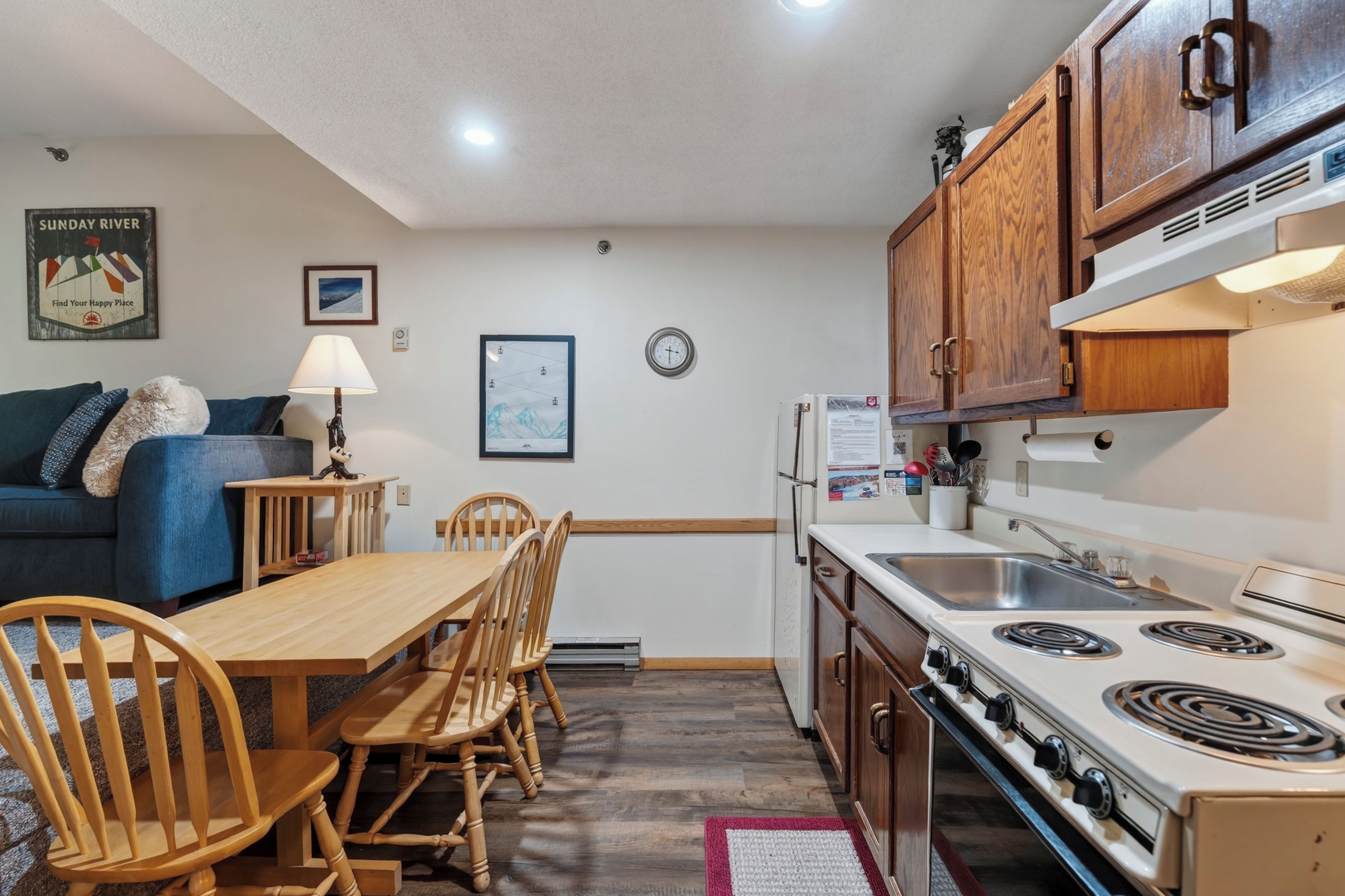 A compact kitchen with wooden cabinets, a stove, and a dining area with a table and chairs.