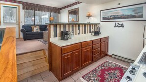 A compact kitchen with a central island, a dining area with a couch, and a framed landscape painting on the wall.