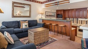 A living room with a sofa, a coffee table, and a kitchen area with a bar and stools.