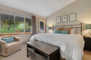 Une chambre avec un grand lit, une chaise, un banc, une table de chevet et une fenêtre donnant sur un paysage verdoyant.