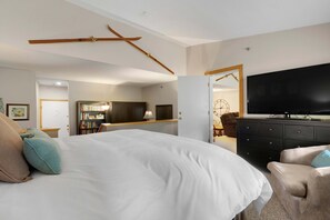 A hotel room with a bed, a television, a desk with a lamp, and a bookshelf.
