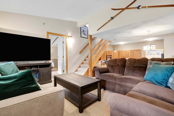 A living room with a sofa, a coffee table, a TV, and a staircase leading to a kitchen.
