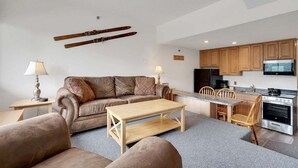 A compact living space with a sofa, coffee table, dining table, and kitchen area. - Ski-In/Ski-Out Sunday River Condo: Sunrise A-133 (Newry)
