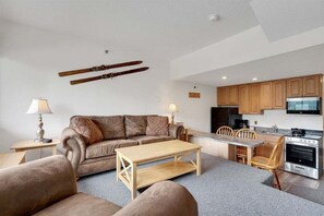 A compact living space with a sofa, coffee table, dining table, and kitchen area. - Ski-In/Ski-Out Sunday River Condo: Sunrise A-133 (Newry)