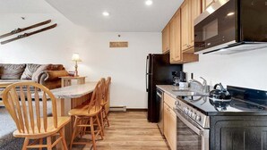 A compact kitchen with wooden cabinets, a stove, a microwave, and a refrigerator. - Ski-In/Ski-Out Sunday River Condo: Sunrise A-133 (Newry)