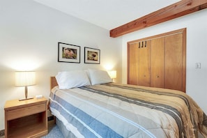 Une chambre à coucher comprenant un lit, une table de chevet, une lampe, une armoire en bois et deux tableaux encadrés accrochés au mur.