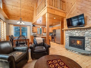 A cozy cabin interior with a stone fireplace, leather chairs, a dining area, and a kitchen. - Sunday River Will View Ski Chalet (Bethel)