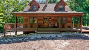 Une cabane en rondins à deux étages, dotée d’un porche, d’une cheminée et de fondations en pierre.