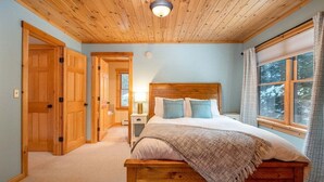 Une chambre à coucher avec un lit en bois, une table de chevet, une lampe, une fenêtre avec des rideaux et une porte.