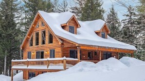 Une cabane en bois, dont le toit est recouvert de neige, entourée d’arbres.