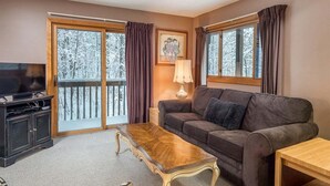 A living room with a sofa, a coffee table, a TV, and a balcony with curtains.