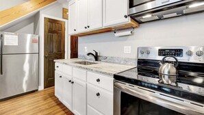 A kitchen with white cabinets, a stainless steel refrigerator, a microwave, and a kettle on the stove.