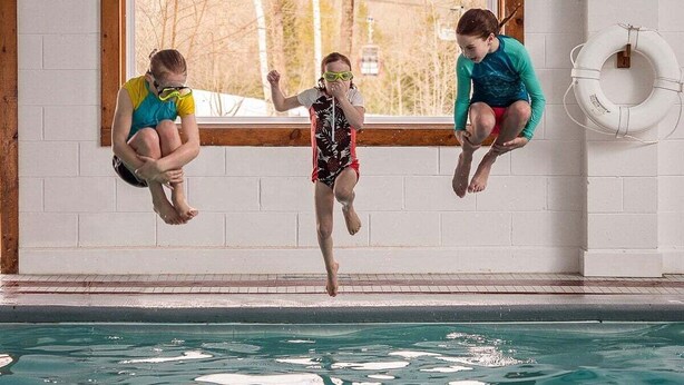 An indoor swimming pool with a diving board and a lifebuoy on the wall.