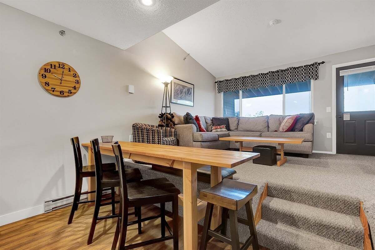 A living room with a wooden dining table, chairs, a sofa, and a staircase.