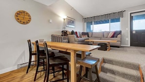 A living room with a wooden dining table, chairs, a sofa, and a staircase.