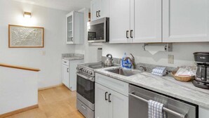 Una cocina moderna con armarios blancos, electrodomésticos de acero inoxidable, una encimera de mármol y un horno empotrado.